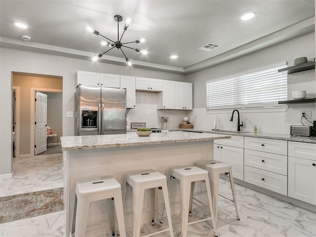 kitchen with marble finish floor, stainless steel refrigerator with ice dispenser, visible vents, a sink, and a kitchen breakfast bar