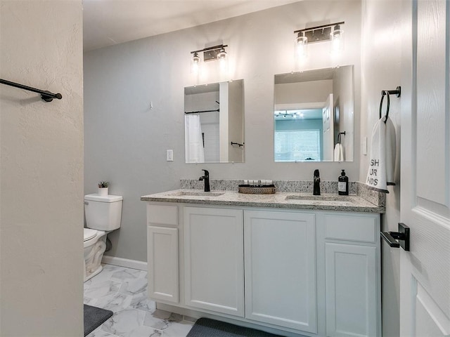 bathroom featuring toilet, marble finish floor, double vanity, and a sink