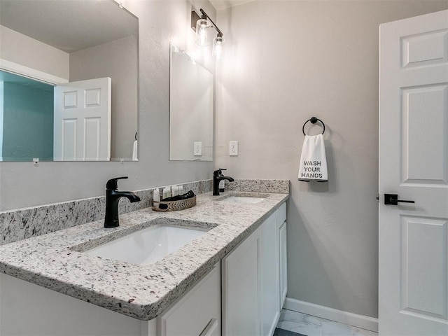 bathroom featuring double vanity, marble finish floor, baseboards, and a sink