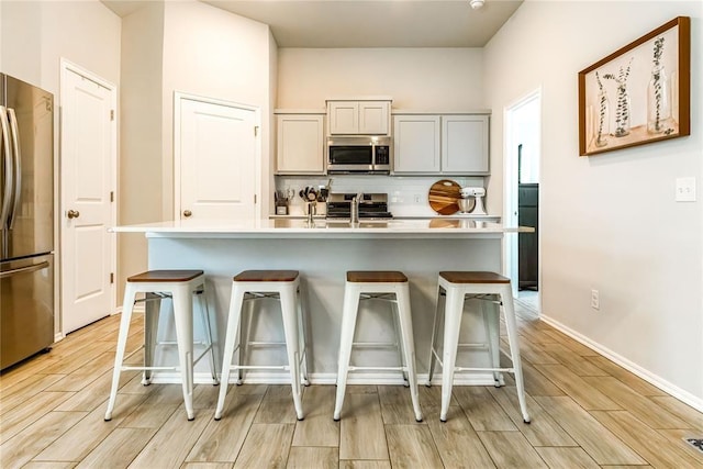 kitchen featuring light countertops, appliances with stainless steel finishes, wood finish floors, and backsplash