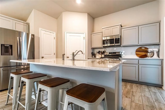 kitchen with stainless steel appliances, tasteful backsplash, gray cabinets, a sink, and an island with sink