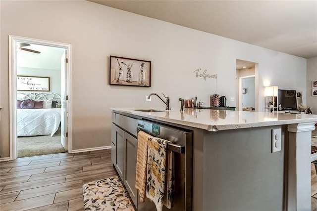 kitchen with dishwasher, light stone counters, wood tiled floor, a kitchen island with sink, and a sink