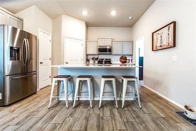 kitchen with stainless steel appliances, a kitchen bar, light countertops, and wood tiled floor