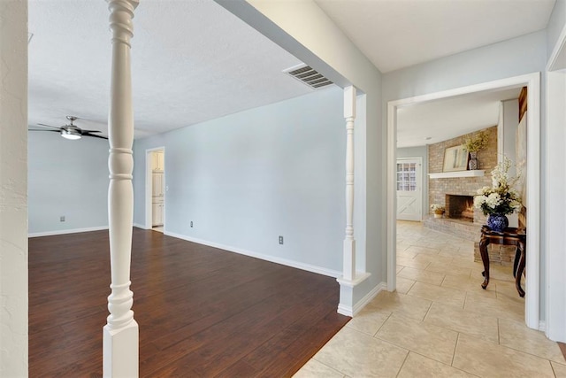 interior space featuring ceiling fan, a fireplace, visible vents, baseboards, and ornate columns