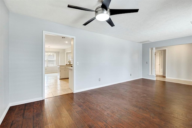 spare room with a textured ceiling, ceiling fan with notable chandelier, wood-type flooring, and baseboards