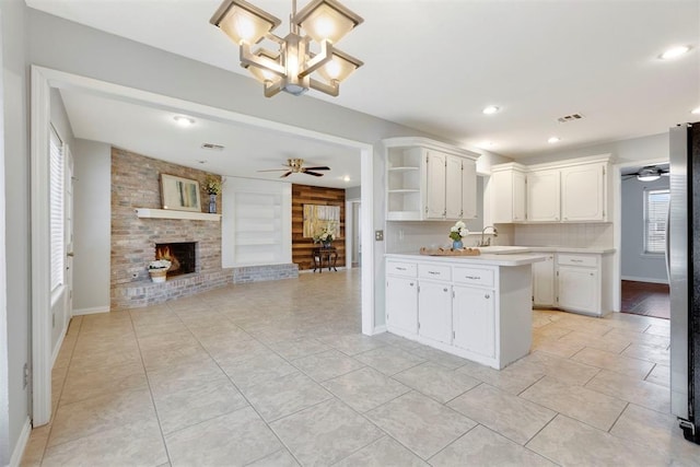 kitchen with ceiling fan with notable chandelier, a peninsula, light countertops, a brick fireplace, and open shelves