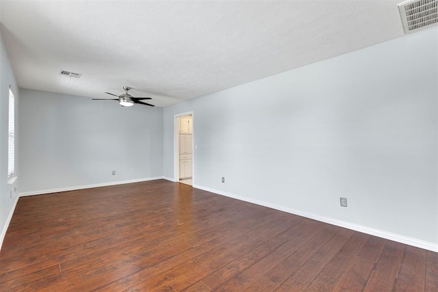 spare room with dark wood-style floors, ceiling fan, visible vents, and baseboards