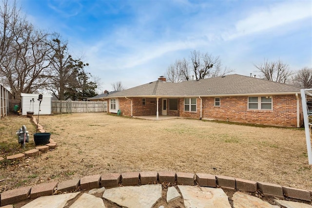 rear view of house with an outbuilding, a patio area, brick siding, and a fenced backyard