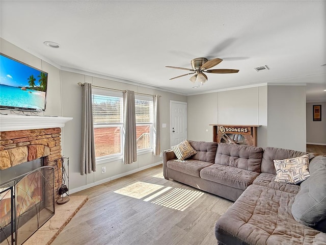 living area with baseboards, visible vents, a ceiling fan, a stone fireplace, and light wood-type flooring