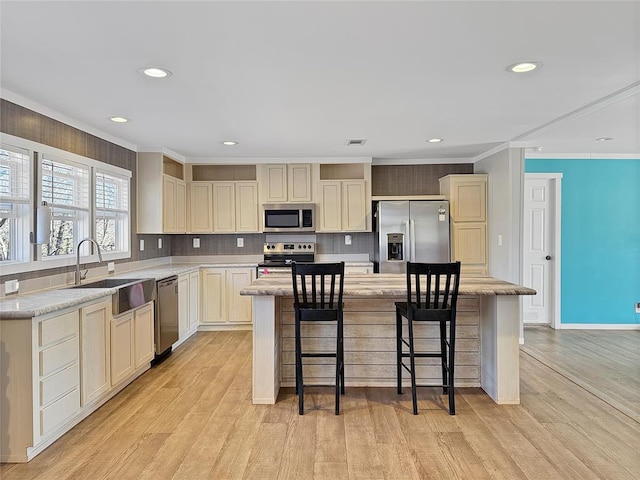 kitchen with appliances with stainless steel finishes, a center island, crown molding, light wood-style floors, and a sink