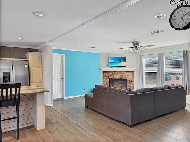 living area with ornamental molding, light wood-type flooring, visible vents, and a fireplace