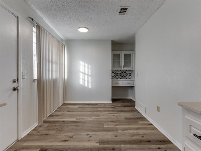 unfurnished dining area featuring baseboards, light wood-style flooring, visible vents, and a textured ceiling