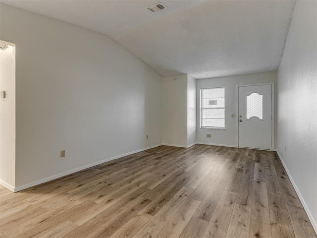 unfurnished living room featuring lofted ceiling, light wood-style flooring, visible vents, and baseboards