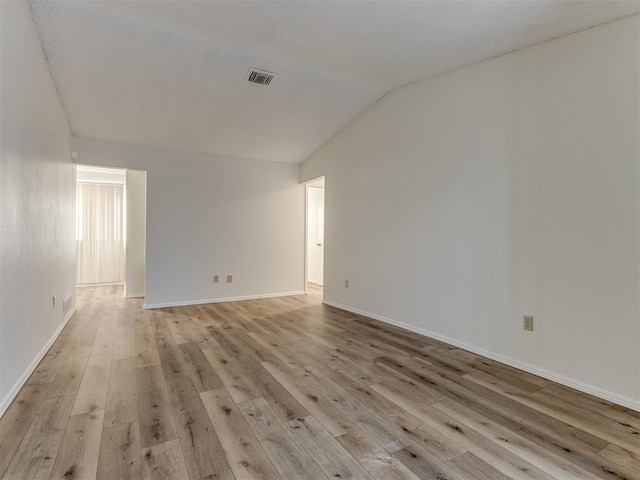 spare room with light wood-style floors, visible vents, vaulted ceiling, and baseboards