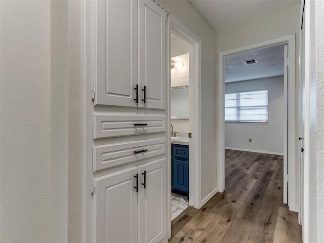 hall featuring baseboards, visible vents, a textured ceiling, light wood-type flooring, and a sink