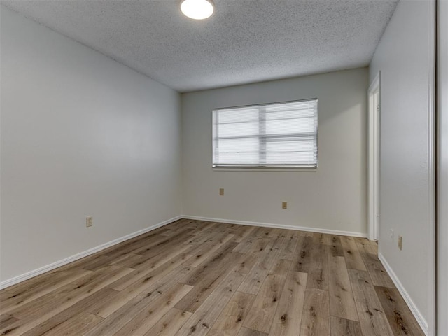 empty room with light wood-style floors, baseboards, and a textured ceiling