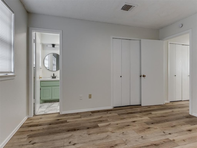 unfurnished bedroom featuring light wood finished floors, baseboards, visible vents, connected bathroom, and a sink