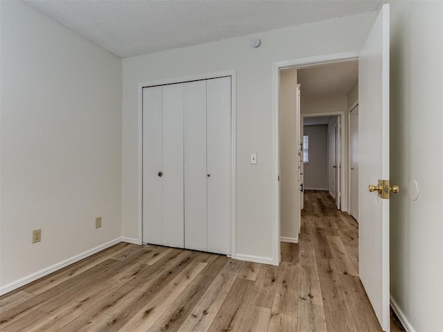 unfurnished bedroom featuring a textured ceiling, a closet, light wood-type flooring, and baseboards