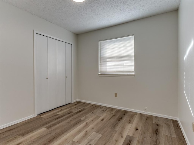 unfurnished bedroom featuring light wood-style floors, a textured ceiling, baseboards, and a closet