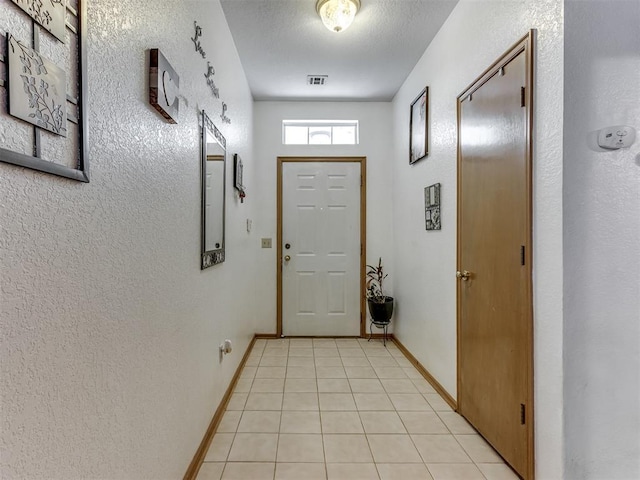 doorway with visible vents, a textured wall, baseboards, and light tile patterned flooring