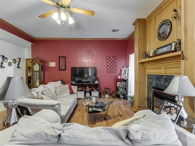 living area featuring visible vents, a tile fireplace, ceiling fan, wood finished floors, and crown molding