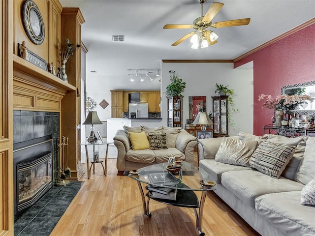 living area with a tile fireplace, crown molding, visible vents, light wood-type flooring, and track lighting