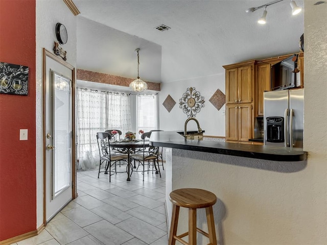 kitchen with a peninsula, visible vents, brown cabinetry, dark countertops, and stainless steel fridge