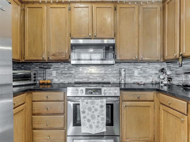 kitchen with dark countertops, a toaster, appliances with stainless steel finishes, and tasteful backsplash