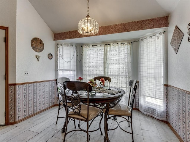 dining area featuring lofted ceiling, baseboards, wainscoting, wallpapered walls, and an inviting chandelier