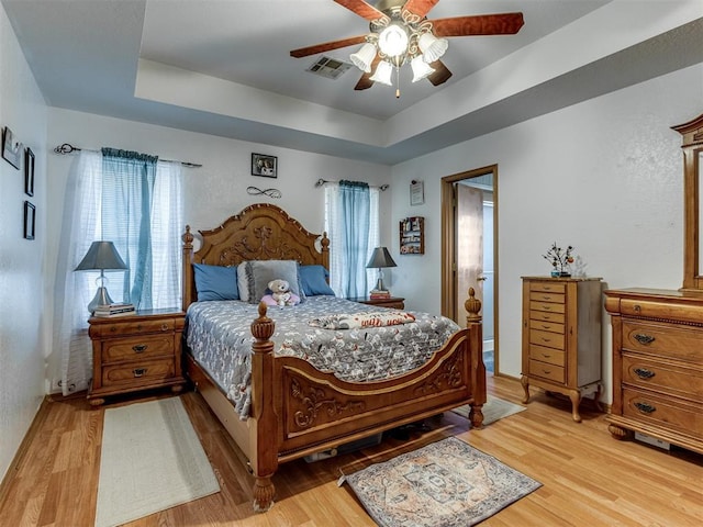 bedroom with ceiling fan, light wood-type flooring, a raised ceiling, and visible vents