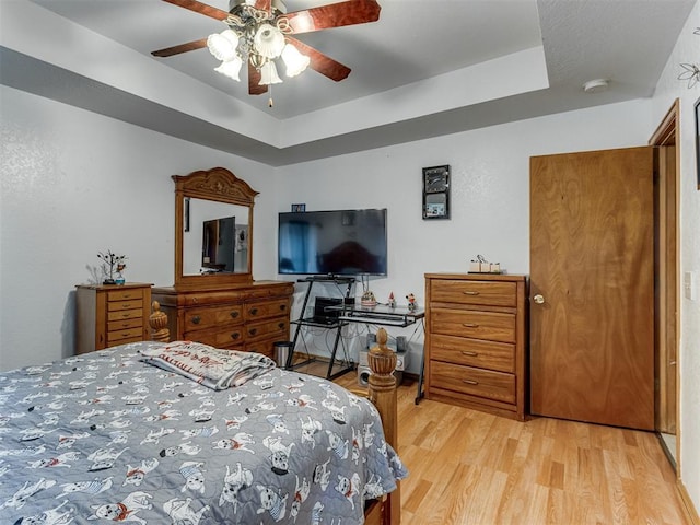 bedroom featuring light wood finished floors, a raised ceiling, and a ceiling fan