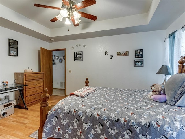 bedroom featuring light wood finished floors, a tray ceiling, visible vents, and a ceiling fan