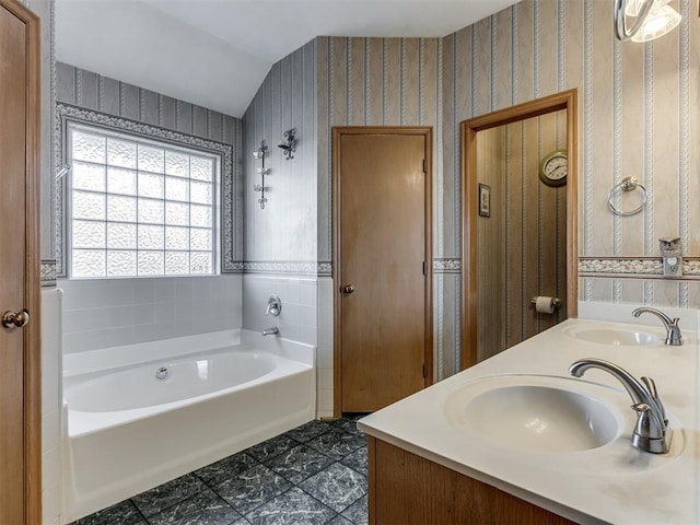 bathroom featuring a garden tub, a sink, and wallpapered walls