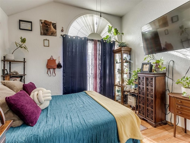 bedroom with lofted ceiling, a textured wall, and wood finished floors