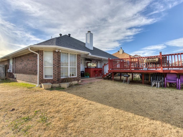 rear view of property featuring a deck, brick siding, a chimney, and a lawn