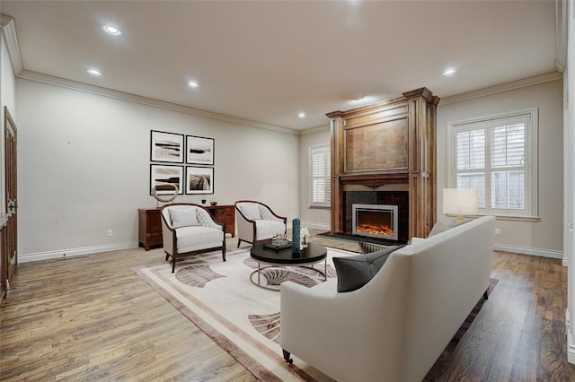 living room with a large fireplace, crown molding, baseboards, and light wood-style floors