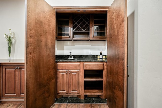 bar with a textured wall, dark wood-type flooring, indoor wet bar, and a sink