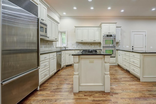 kitchen with tasteful backsplash, dark countertops, light wood-style floors, a kitchen island, and built in appliances