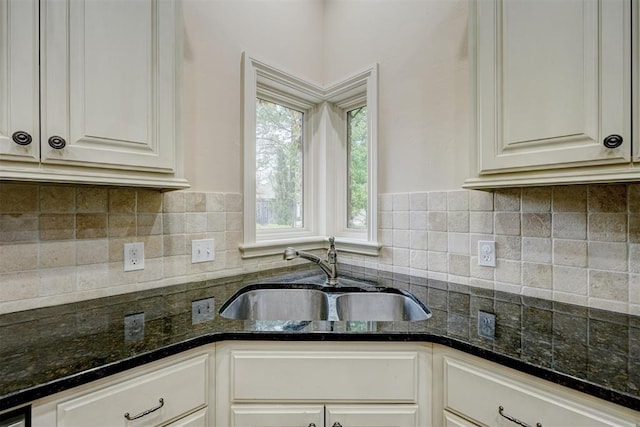 kitchen with tasteful backsplash, dark stone countertops, a sink, and white cabinets