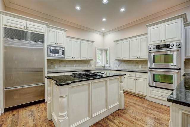 kitchen featuring ornamental molding, light wood-style flooring, dark stone countertops, and built in appliances