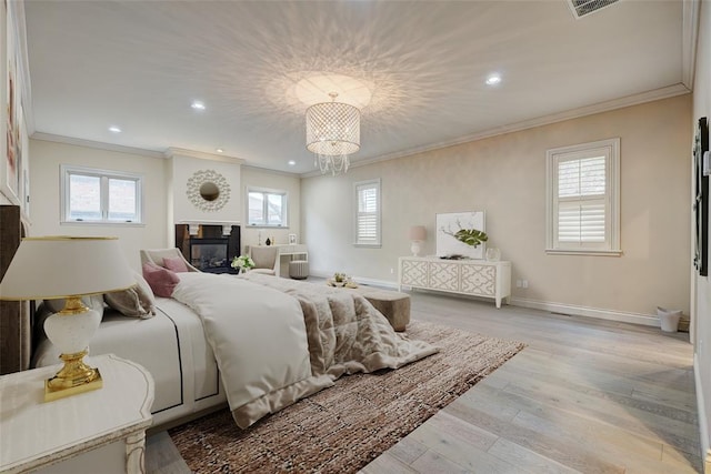 bedroom featuring light wood finished floors, visible vents, ornamental molding, a glass covered fireplace, and baseboards