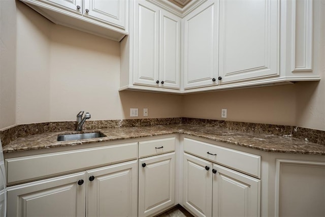 kitchen with dark stone counters, a sink, and white cabinetry