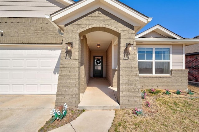 entrance to property featuring a garage, concrete driveway, and brick siding