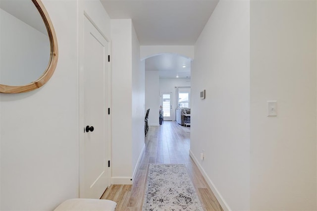 corridor with light wood-type flooring, arched walkways, and baseboards