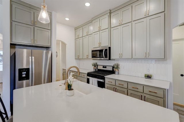 kitchen with arched walkways, tasteful backsplash, light countertops, appliances with stainless steel finishes, and a sink