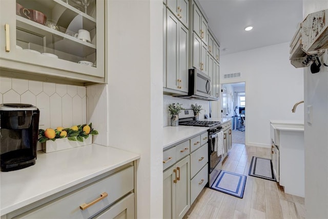 kitchen featuring light countertops, appliances with stainless steel finishes, light wood finished floors, glass insert cabinets, and tasteful backsplash