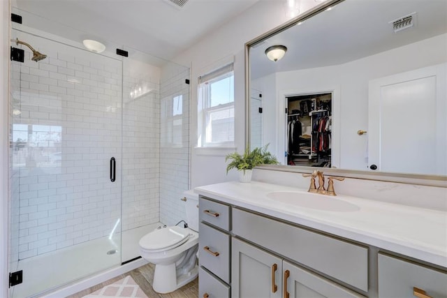 bathroom featuring toilet, vanity, visible vents, a spacious closet, and a shower stall