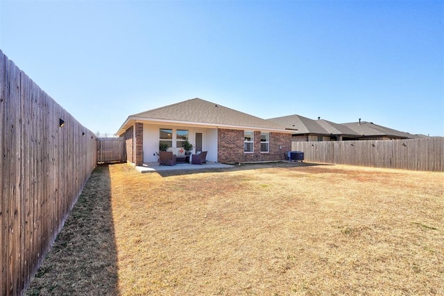 rear view of property featuring a lawn, a patio, a fenced backyard, central air condition unit, and brick siding