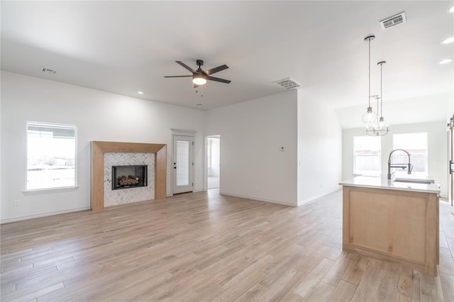 unfurnished living room with visible vents, a sink, light wood-style floors, a fireplace, and ceiling fan