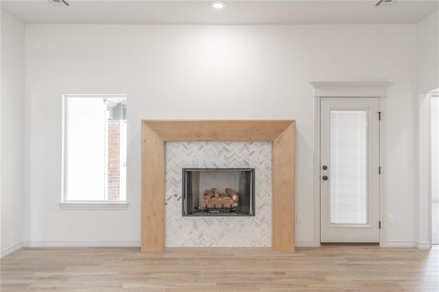 unfurnished living room with a tiled fireplace, visible vents, wood finished floors, and baseboards